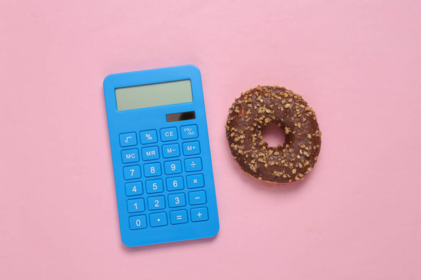 Kalorienzählen. Taschenrechner und kalorienreicher Donut auf rosa Hintergrund  - Foto, Bild