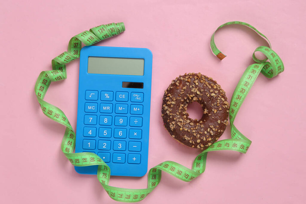 Calorie counting. Calculator and measuring tape, high calorie donut on pink background - Fotoğraf, Görsel