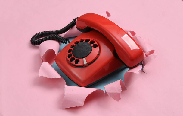 Ретро ротационный телефон через разорванную дыру на сине-розовом пастельном фоне. Концептуальное искусство. Пастельный цветовой тренд. Минимализм - Фото, изображение