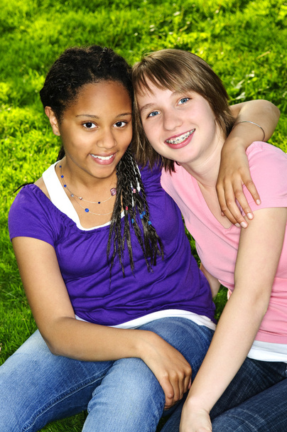 Two teenage girls sitting on grass and hugging - Photo, Image