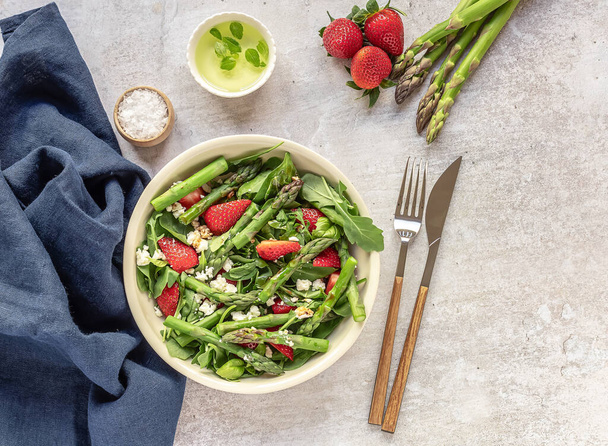 Een gezonde en heerlijke salade gemaakt van verse aardbeien, groene asperges, feta kaas met groentebladeren.  - Foto, afbeelding