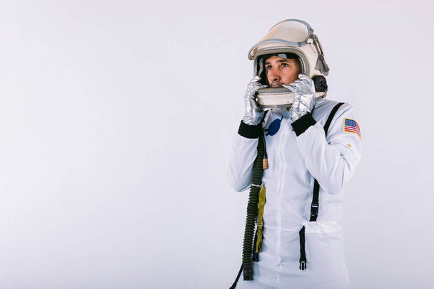 Mannelijke kosmonaut in ruimtepak en helm, helm met handen vasthoudend, op witte achtergrond. - Foto, afbeelding