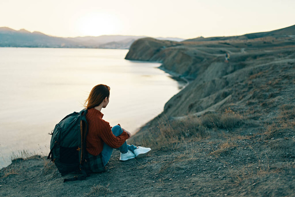 nainen patikoija istuu maassa vuorilla lähellä merta auringonlaskun aikaan - Valokuva, kuva