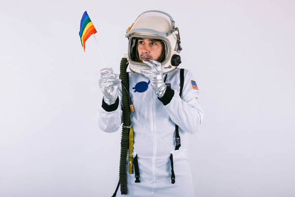 gay macho cosmonauta en espacio traje y casco celebración lgtbi arco iris bandera en blanco fondo. - Foto, imagen