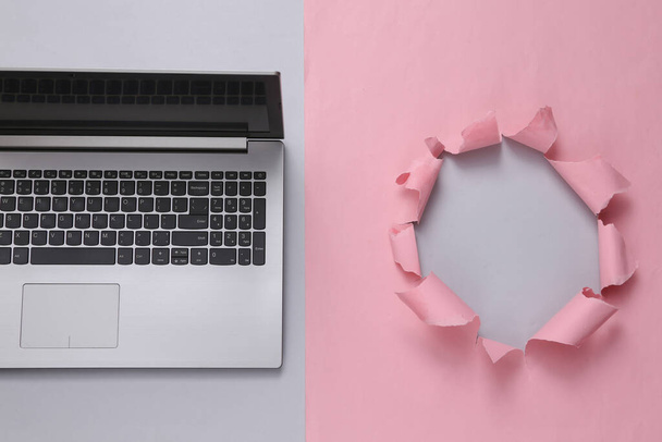 Laptop on pink background with torn hole. Copy space - Zdjęcie, obraz