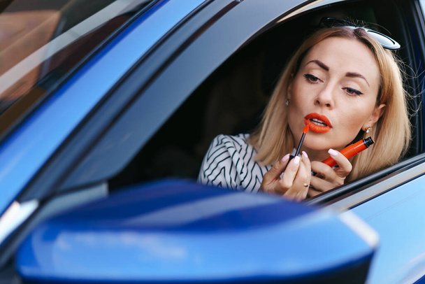Женщина смотрит в боковое зеркало машин и красит губы - Фото, изображение