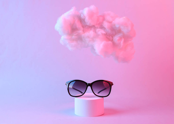 Sonnenbrillen mit schwebenden, flauschigen Wolken in rosa-blauem Neonlicht. Schönheit und Mode. Konzeptkunst. Minimalistische Idee  - Foto, Bild