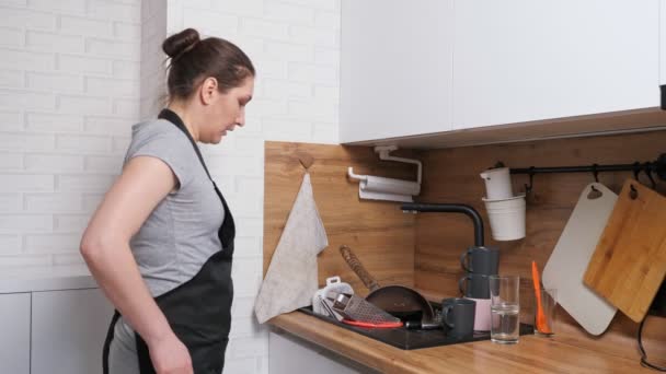 Αναστατωμένη γυναίκα έρχεται στην κουζίνα και βλέπει βρώμικα πιάτα στο νεροχύτη - Πλάνα, βίντεο