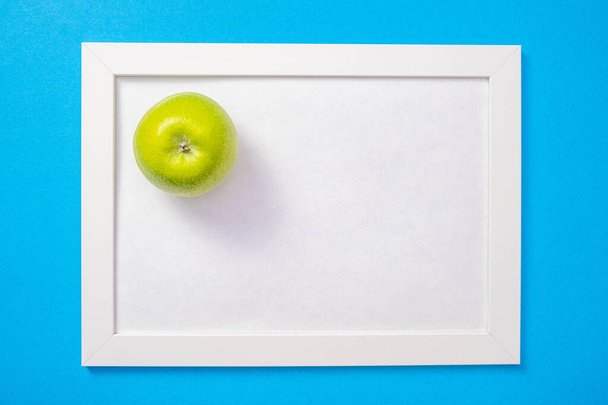 a green apple lies on a white frame with a white background, general blue background - Photo, Image