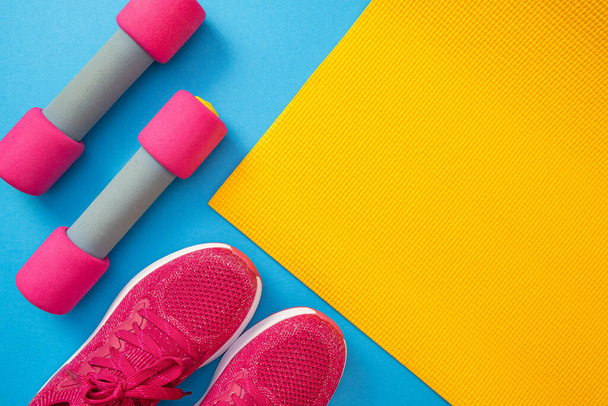 pink sneakers and yellow mat, dumbbells, blue background and close-up - Φωτογραφία, εικόνα