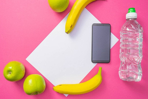 vitamins - apples and bananas, a cell phone and a bottle of water, lie on a common pink background - Photo, Image
