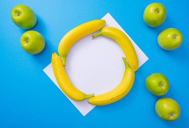 white sheet of paper, six apples and four bananas lie on a common blue background - Photo, Image