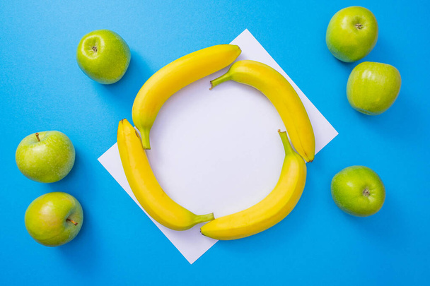 white sheet of paper, six apples and four bananas lie in a circle on a common blue background - Photo, Image