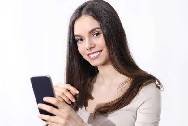  Mujer joven sosteniendo un teléfono inteligente mirando a la cámara y sonriendo sobre fondo blanco - Foto, Imagen