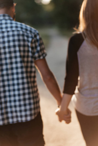 Widok z tyłu dwóch sylwetek trzymających się za ręce i spacerujących razem, patrzących na siebie na randce o zachodzie słońca w lecie. Zdjęcie jest nieostre. Kontekst tekstu. - Zdjęcie, obraz