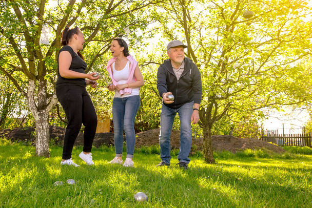 Frohe, positiv lächelnde Familie, die während eines schönen Sommertages im Freien im Garten ein traditionelles französisches Boule-Spiel spielt und die Freizeit genießt  - Foto, Bild