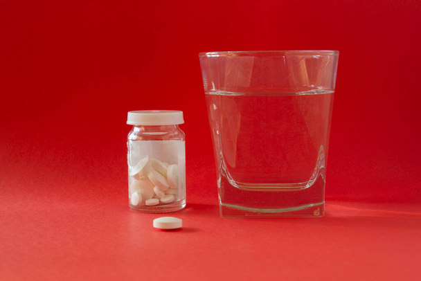 Egy pohár vizet, üveget, gyógyszereket, tablettákat, drogokat. Elszigetelt. piros háttér. - Fotó, kép