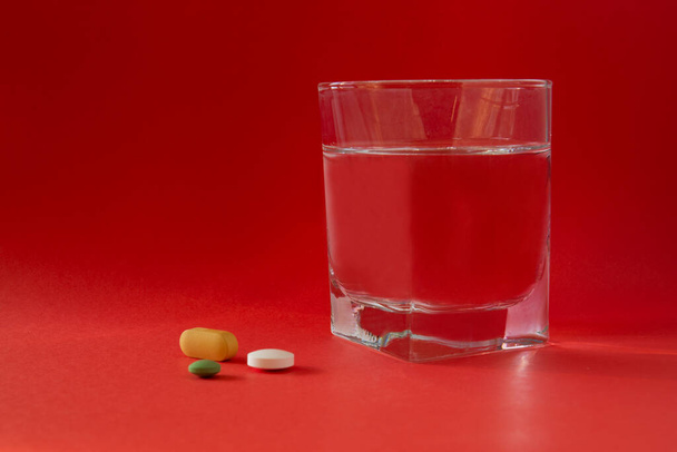 um copo de água e medicamentos, comprimidos, drogas. isolado. Fundo vermelho. - Foto, Imagem