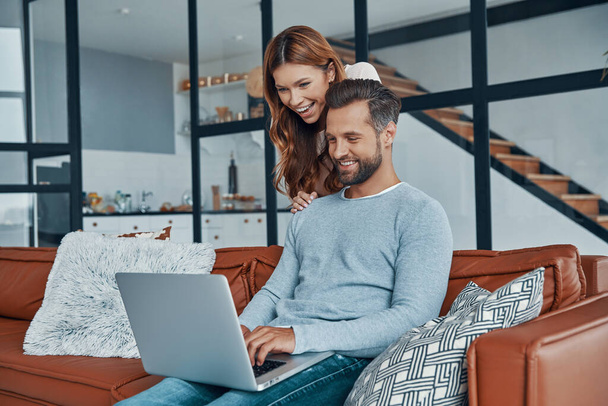 Cheerful young couple using laptop and smiling while spending time at home - Photo, image