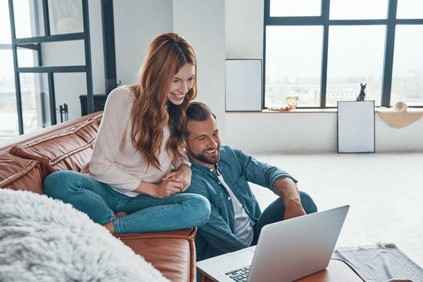 Loving young couple using laptop and smiling while spending time at home - Foto, Imagen