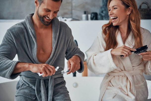Loving young couple in bathrobes laughing while doing morning routine - Foto, imagen