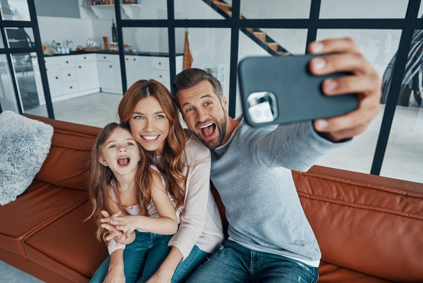 Playful young family smiling and making selfie while spending time at home - Фото, изображение