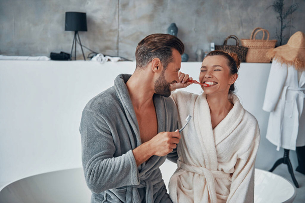 Beautiful young couple in bathrobes cleaning teeth while doing morning routine - Foto, immagini
