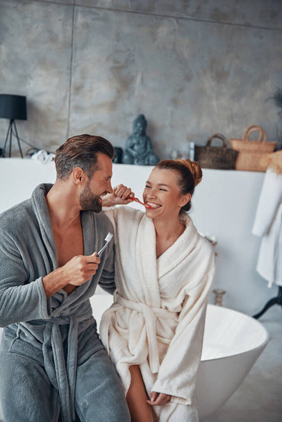 Happy young couple in bathrobes cleaning teeth while doing morning routine - Valokuva, kuva