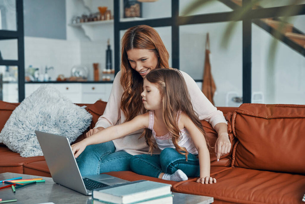 Mother and her daughter bonding together and smiling while using laptop at home - Фото, изображение