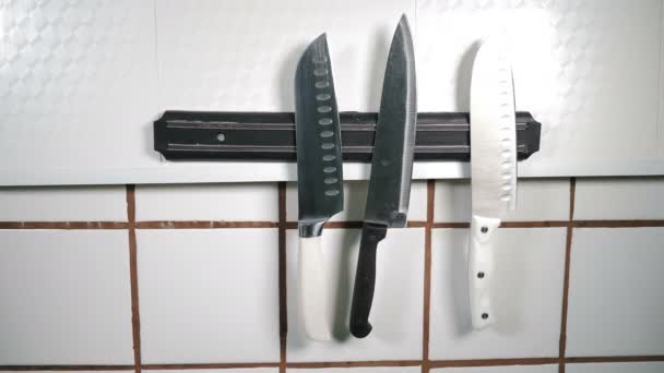 Kések mágnesre állítva a falon az éttermi konyhában. konyhai eszközök lógnak mágneses tartó. A fekete kesztyűs séf egy kést helyez el. Főzési eszközök. Különböző éles kések használatra kész. 4 k - Felvétel, videó