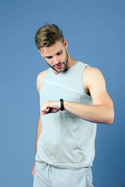 Sportsman look at fitness watch on violet background. Man with sport smartwatch in blue sportswear. Track activity and workout. New technology for healthy lifestyle. Sport or fitness and wellness - Fotografie, Obrázek