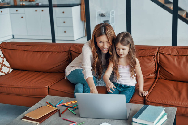 Mother and her daughter bonding together and smiling while using laptop at home - Фото, изображение