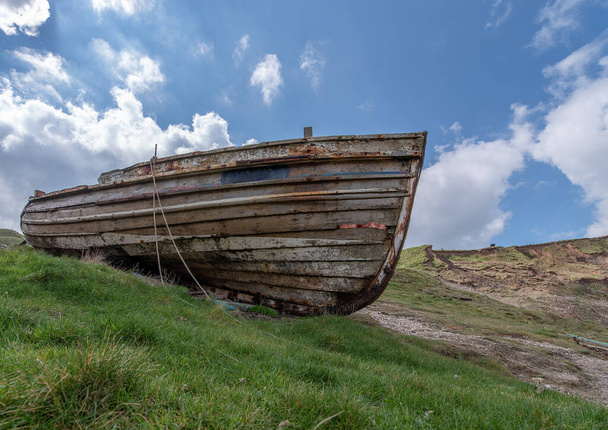 Um barco de pesca de madeira angustiado encalhado no banqueiro grama no dia ensolarado com fundo azul céu. - Foto, Imagem