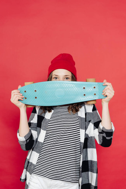 Belle adolescente posant avec penny board sur fond rouge - Photo, image