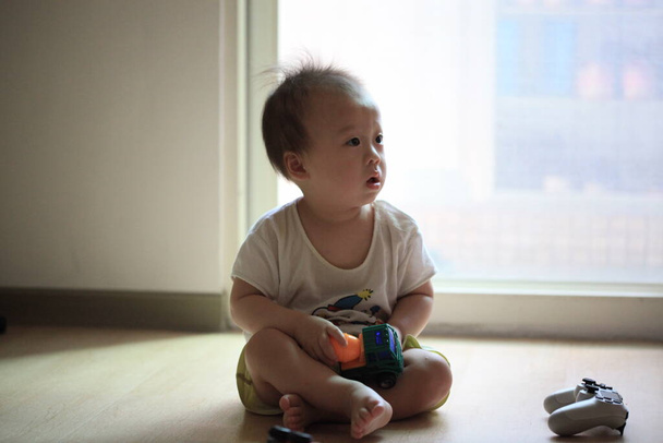 Kisbaba ül a nappaliban, kezében egy játékautóval. - Fotó, kép