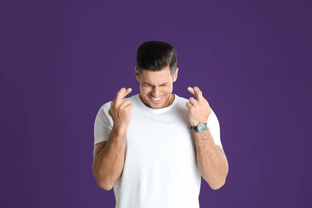 Man with crossed fingers on purple background. Superstition concept - Foto, Bild
