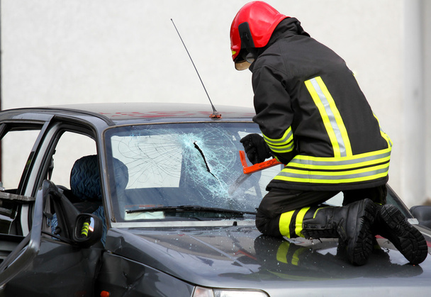 πυροσβέστης με γάντια εργασίας, σπάζοντας ένα αυτοκίνητο παρμπρίζ να παρουσιάζει ενδιαφέρον - Φωτογραφία, εικόνα