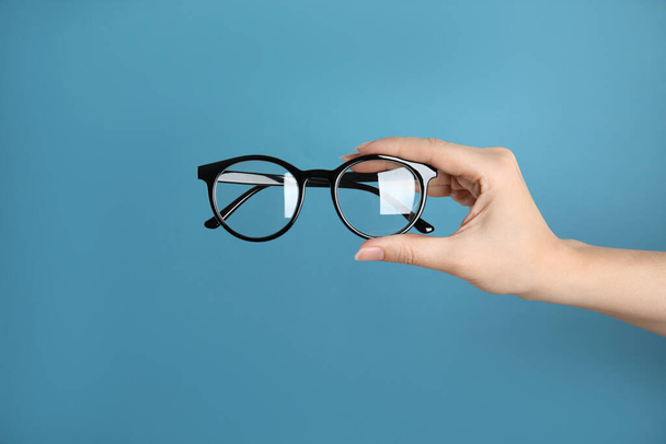 Woman holding glasses on blue background, closeup. Ophthalmologist prescription - Φωτογραφία, εικόνα