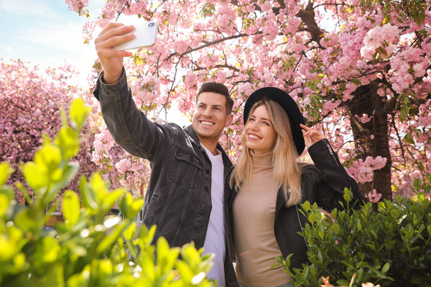 Happy couple taking selfie near blossoming sakura outdoors on spring day - Фото, изображение