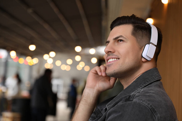 Handsome man with headphones listening to music in outdoor cafe, space for text - Fotografie, Obrázek