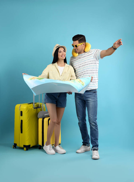 Couple of tourists with map and suitcases on light blue background - Foto, afbeelding