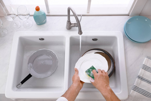 Man washing plate above sink in kitchen, closeup - Foto, Bild