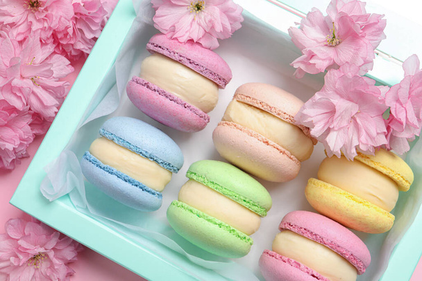 Many delicious colorful macarons in box and flowers on pink background, flat lay - Photo, Image