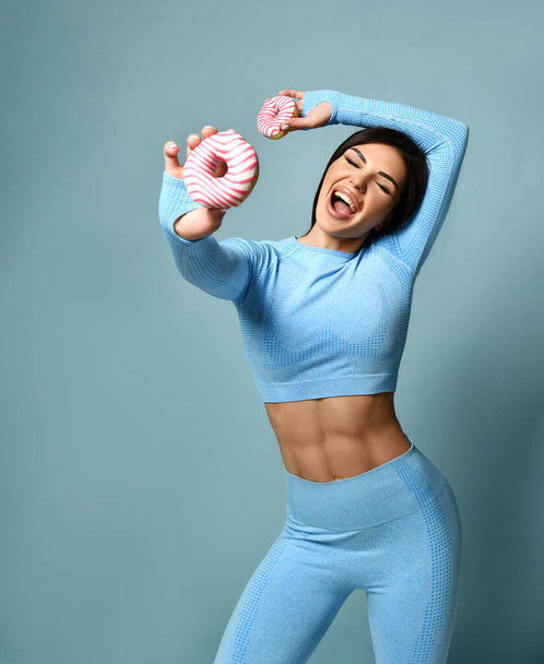 Pensive and dreamy brunette fitness girl looking sweetly at donut, thinking about calories, standing in sportswear - Foto, afbeelding