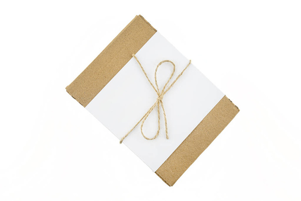 Ένα μικρό χάρτινο κουτί από κυματοειδές χαρτόνι τυλιγμένο με ένα λευκό φύλλο και μια γκρι χορδή σε ένα τόξο, απομονωμένο σε λευκό φόντο, πάνω όψη. - Φωτογραφία, εικόνα