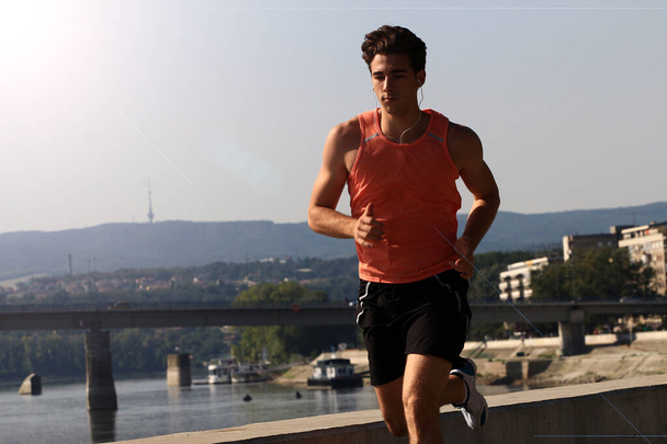 セルビアのノヴィ・サドでドナウ川のほとりを走る若い男性選手。ランナーの肖像画。健康的なライフスタイル、アウトドアランニング、スポーツコンセプト. - 写真・画像