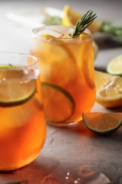 Iced tea with lemon, lime and ice garnished with rosemary twigs. Frozen glasses with citrus slices. Selective focus. - Foto, Imagem