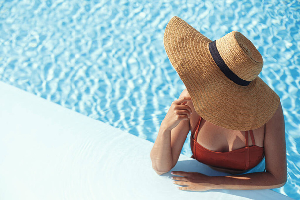 Насолоджуйся літніми канікулами. Красива жінка в капелюсі відпочиває у блакитній воді басейну. Тонка молода жінка купається і відпочиває на краю басейну, вид зверху. Відпочинок і подорожі. Простір для тексту
 - Фото, зображення