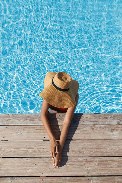 Mulher bronzeada bonita em chapéu relaxante na água da piscina no cais de madeira, desfrutando de férias de verão, vista superior. Magro jovem banho de sol feminino na borda elegante da piscina. Espaço para SMS. Viagens e Feriados - Foto, Imagem