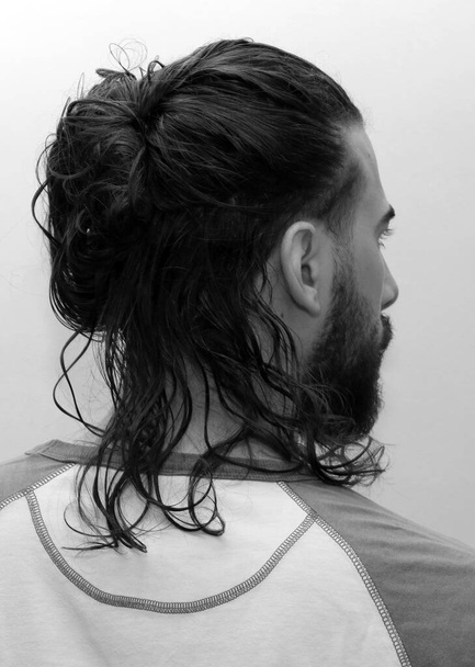 Aantrekkelijk mannelijk model met lang haar en baard poserend in studio op geïsoleerde achtergrond. Stijl, trends, modeconcept. - Foto, afbeelding
